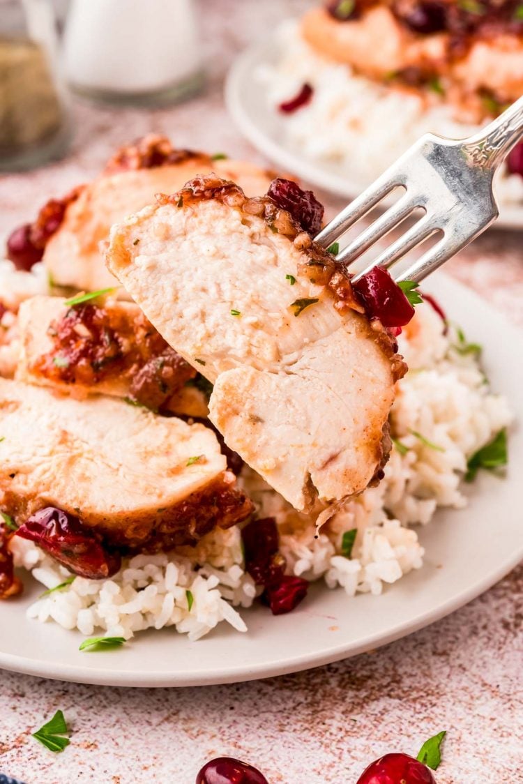 A fork lifting a bite of cranberry chicken away from the dinner plate.