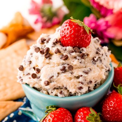 Close up photo of a teal bowl filled with cannoli dip surrounded by crackers and strawberries.