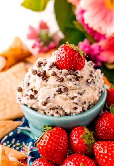 Close up photo of a teal bowl filled with cannoli dip surrounded by crackers and strawberries.