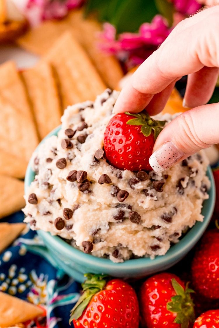 A woman's hand dipping a strawberry in a dessert dip with mini chocolate chips.