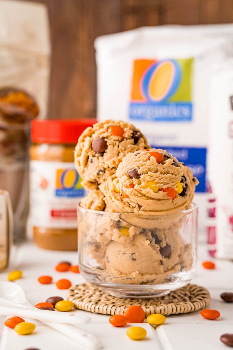 Edible cookie dough in a glass bowl with ingredients behind it.