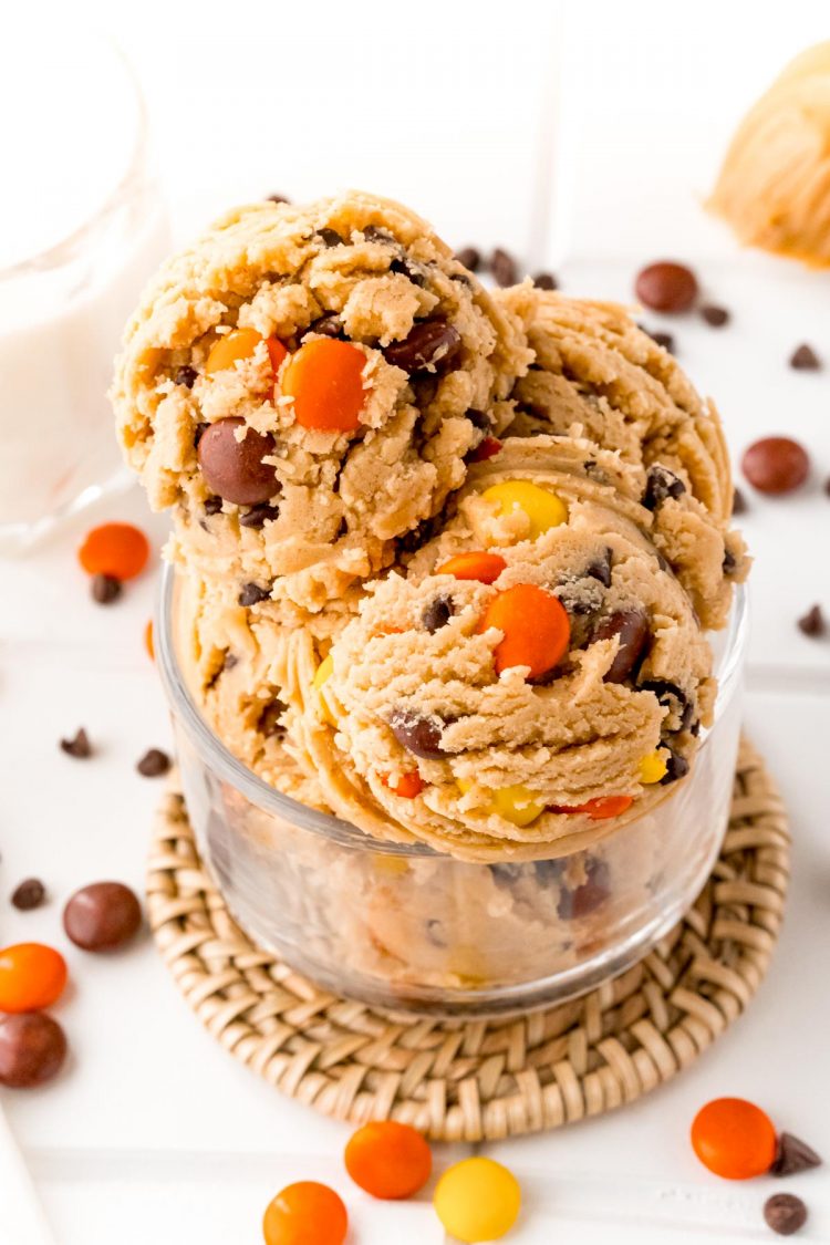 Close up photo of scoops of edible peanut butter cookie dough in a glass bowl on a what table.