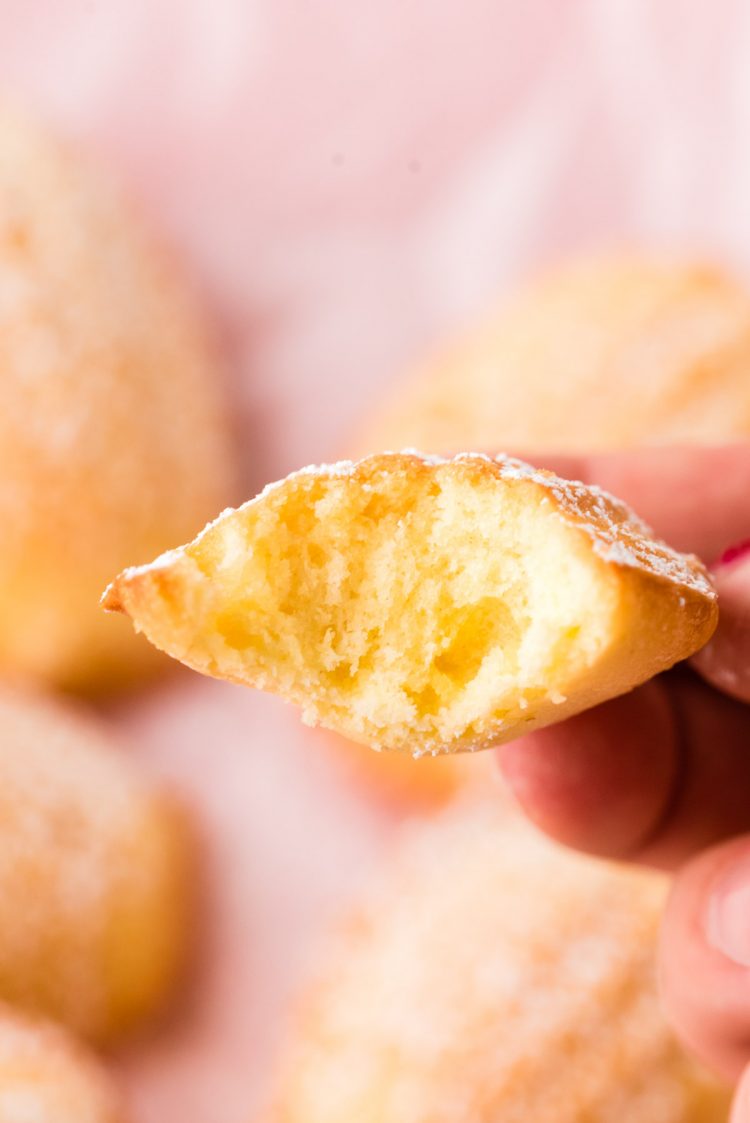 A woman's hand holding a French madeleine with a bite taken out of it.