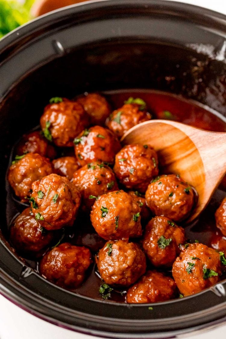 A wooden spoon in a crockpot filled with meatballs.