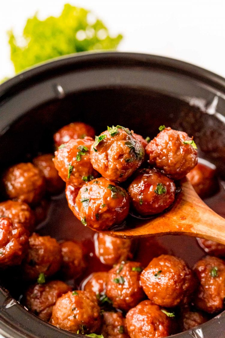 A wooden spoon scooping meatballs out of a crockpot.