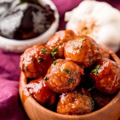 Close up photo of grape jelly meatballs in a brown bowl.
