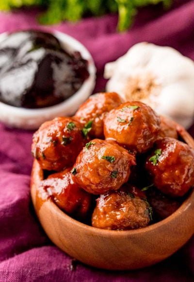 Close up photo of grape jelly meatballs in a brown bowl.