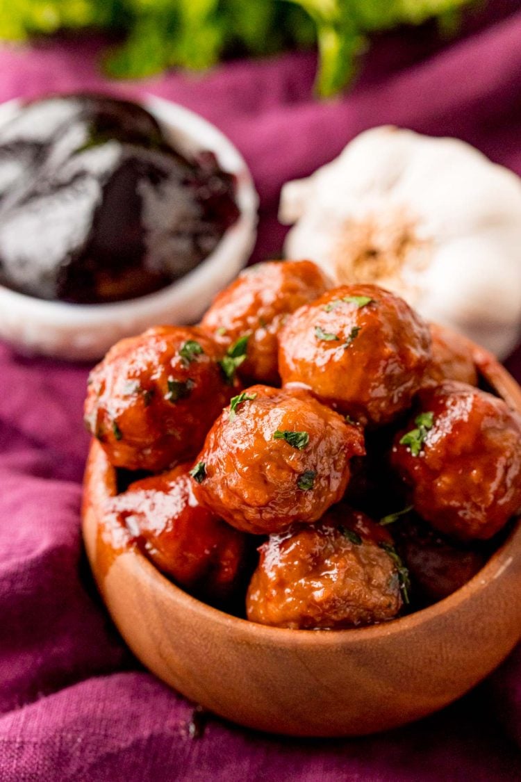 Close up photo of grape jelly meatballs in a brown bowl.