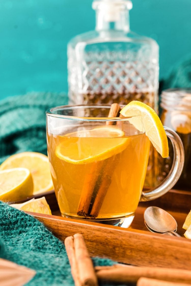A hot toddy garnished with lemon in a clear glass mug on a wooden tray.