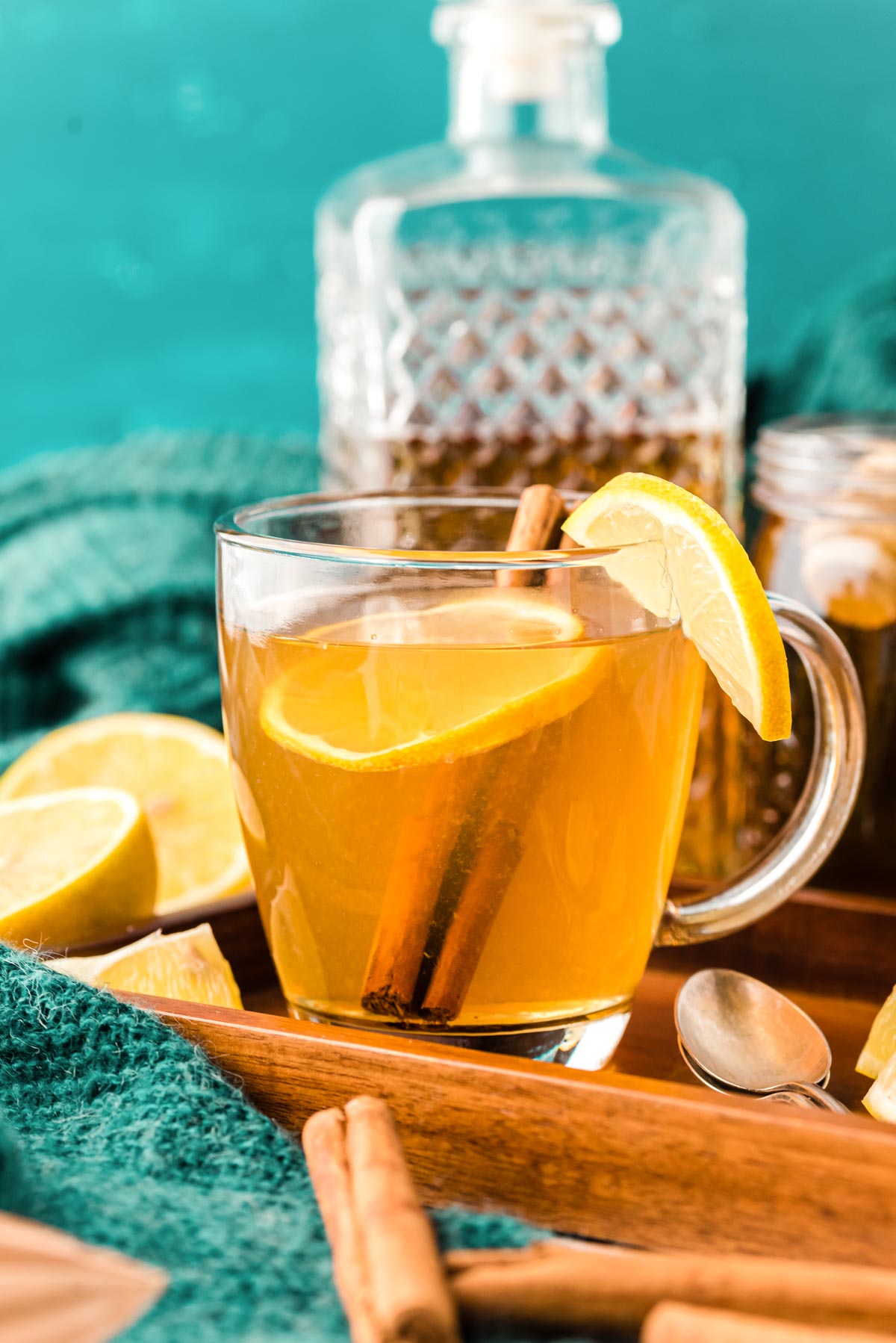 A hot toddy garnished with lemon in a clear glass mug on a wooden tray.
