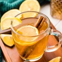 A hot toddy in a clear glass mug with lemon slice and cinnamon stick.