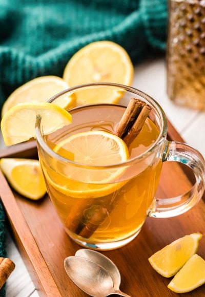 A hot toddy in a clear glass mug with lemon slice and cinnamon stick.