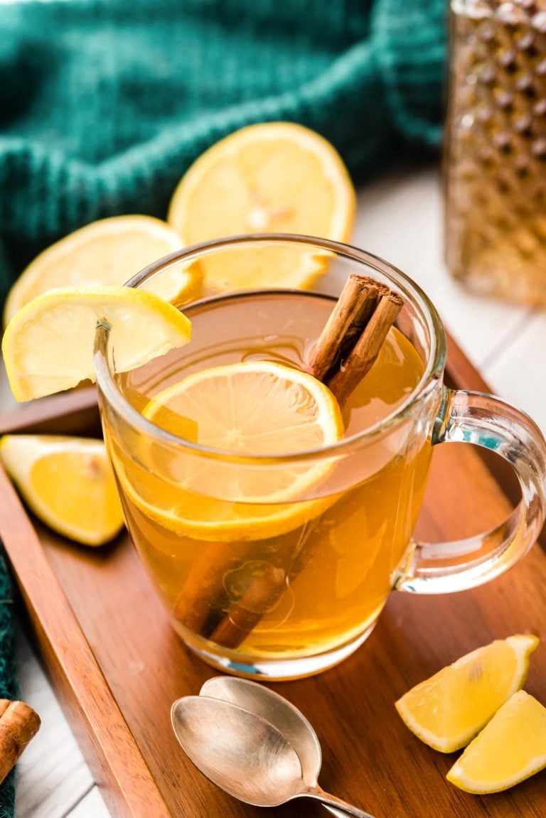 A hot toddy in a clear glass mug with lemon slice and cinnamon stick.