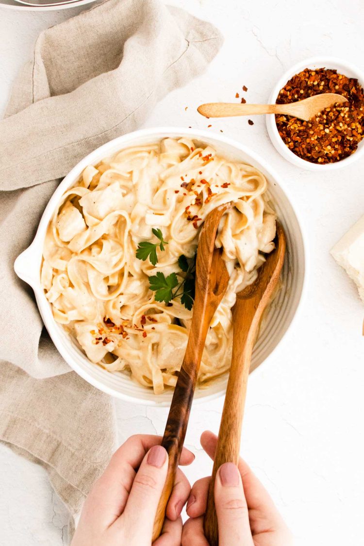 A woman using serving spoons to serve chicken alfredo.