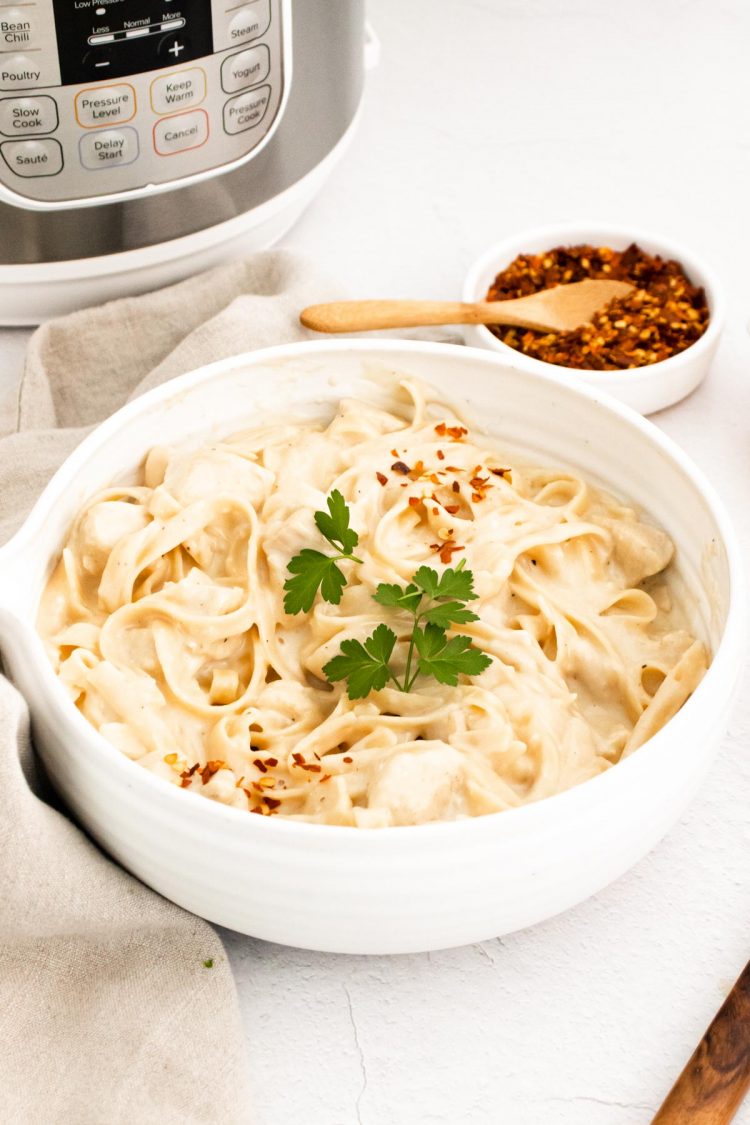 A white bowl of chicken alfredo in front of an instant pot.