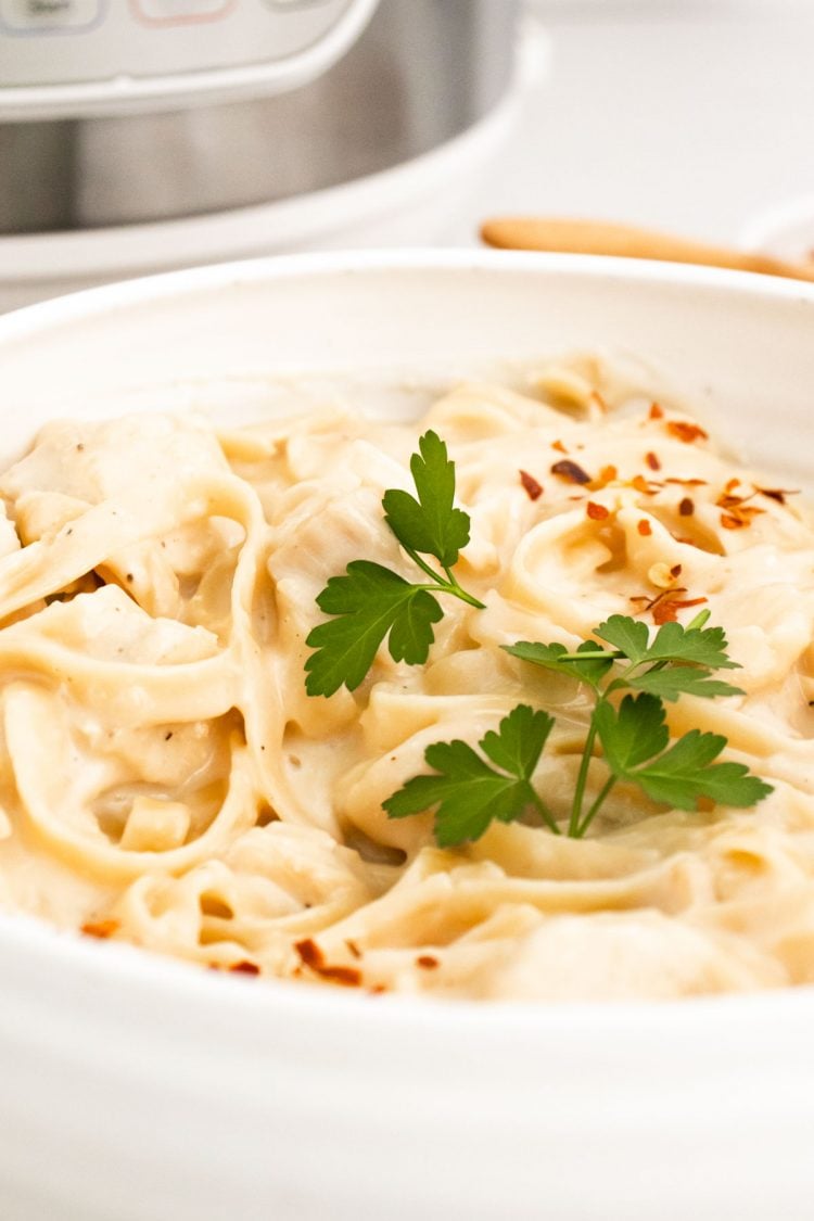 Close up photo of a bowl of fettuccine alfredo in front of an instant pot.