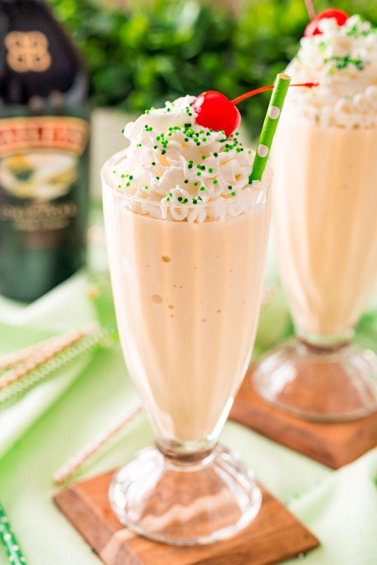 Close up photo of a milkshake glass filled with a Bailey's milkshake and topped with whipped cream and a cherry on a green napkin.