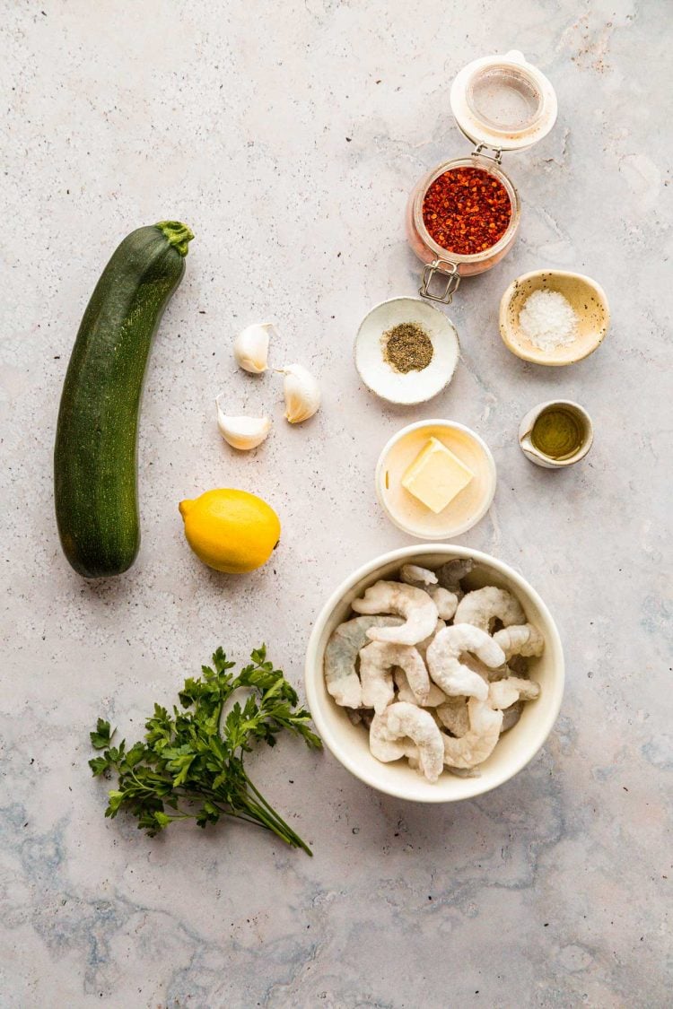 Overhead photo of ingredients to make garlic shrimp with zoodles on grey counter.