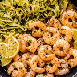 Close up photo of lemon garlic shrimp in a skillet with zucchini noodles and lemon wedges.
