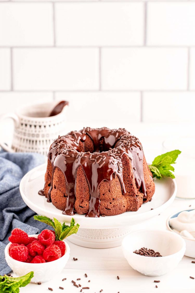 Air fryer chocolate cake on a white cake stand with raspberries in a bowl to the side.