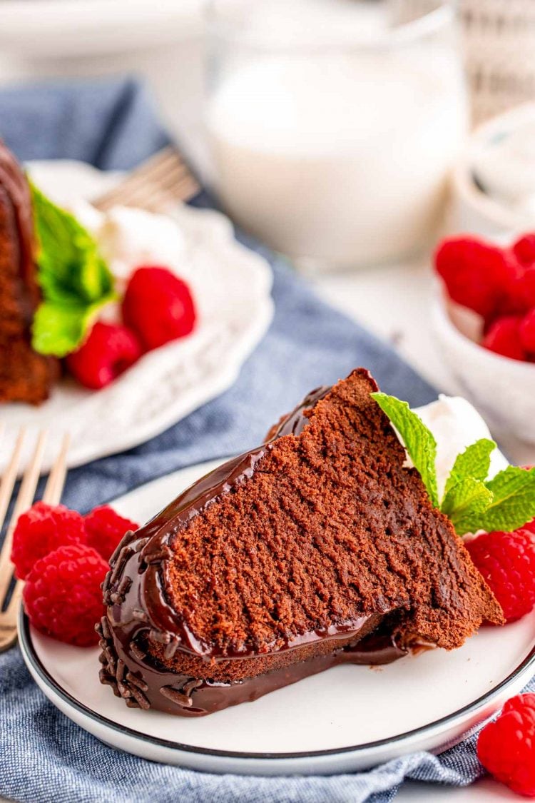 A slice of air fryer chocolate cake on a white plate on a blue napkin garnished with raspberries.