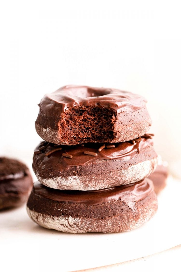 A stack of three chocolate donuts with a bite taken out of the top one.