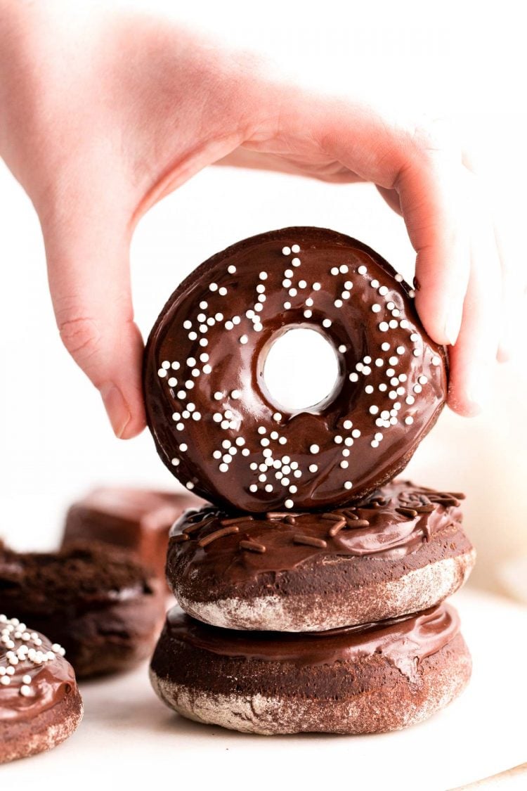 A woman's hand grabbing a chocolate donut off a stack.