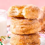 Three cinnamon sugar donuts stacked on top of each other with a bite taken out of the top one.