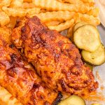 Close up photo of Nashville hot chicken with pickles and fries.