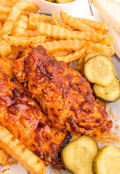 Close up photo of Nashville hot chicken with pickles and fries.