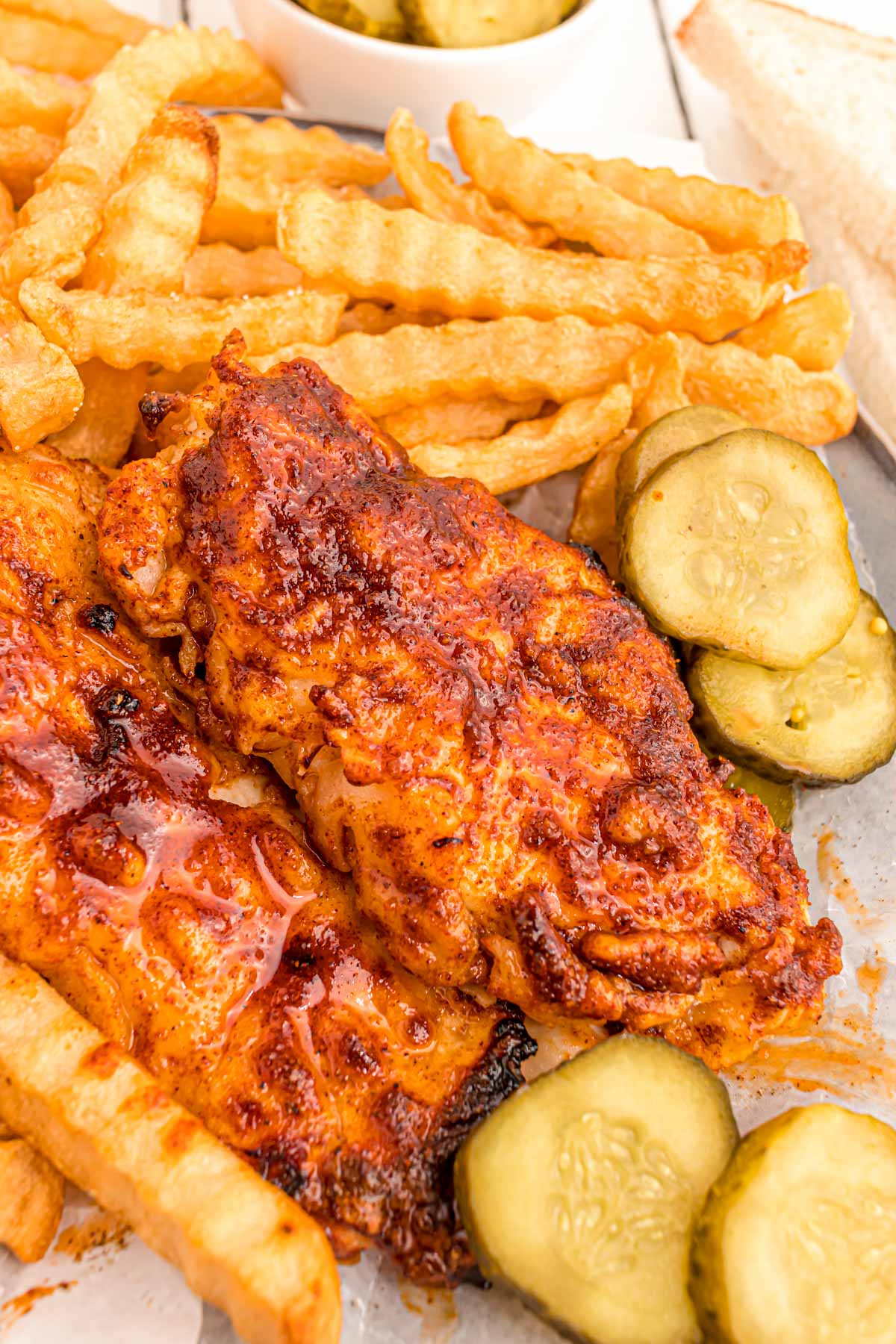 Close up photo of Nashville hot chicken with pickles and fries.