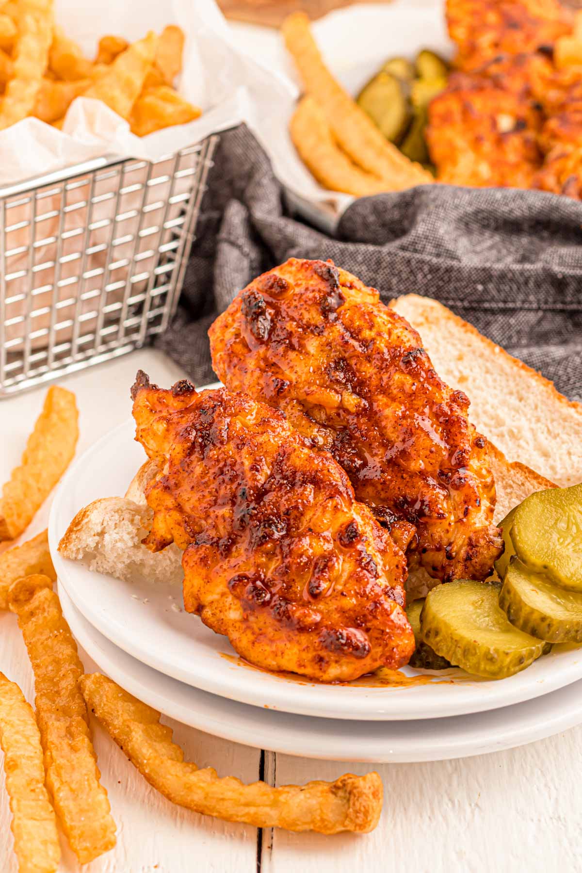 Nashville hot chicken tenders on a white plate with pickles and fries.