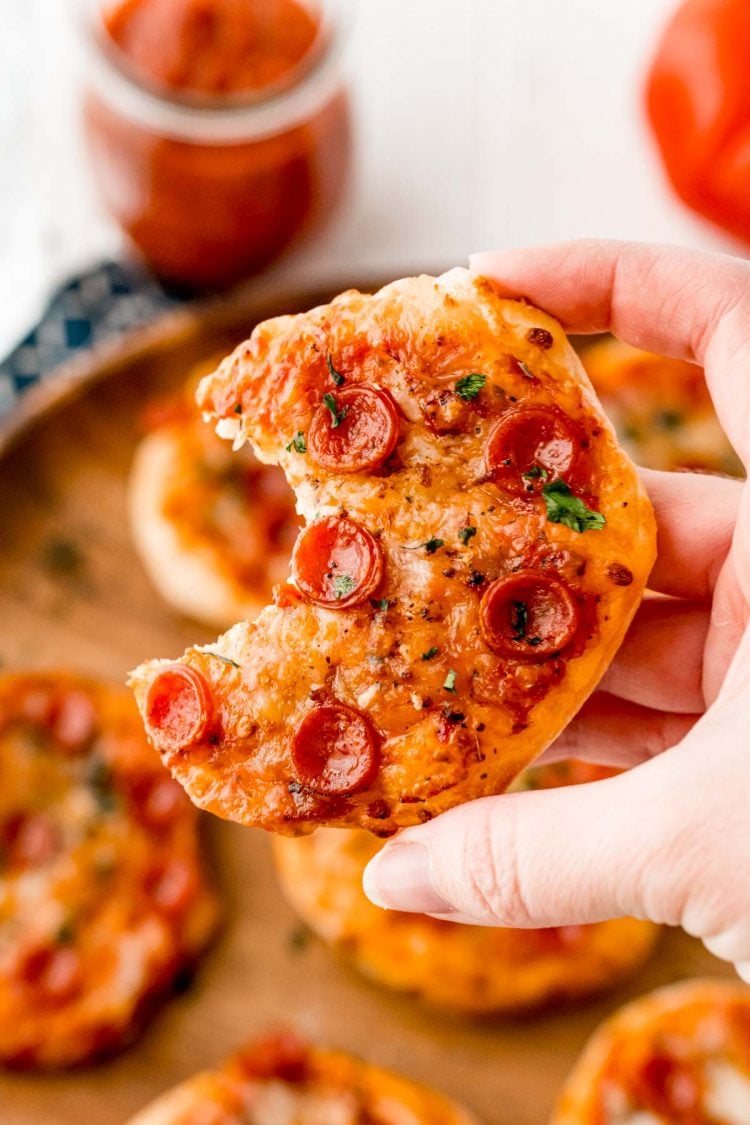 A woman's hand holding a mini pizza with a bite taken out of it.