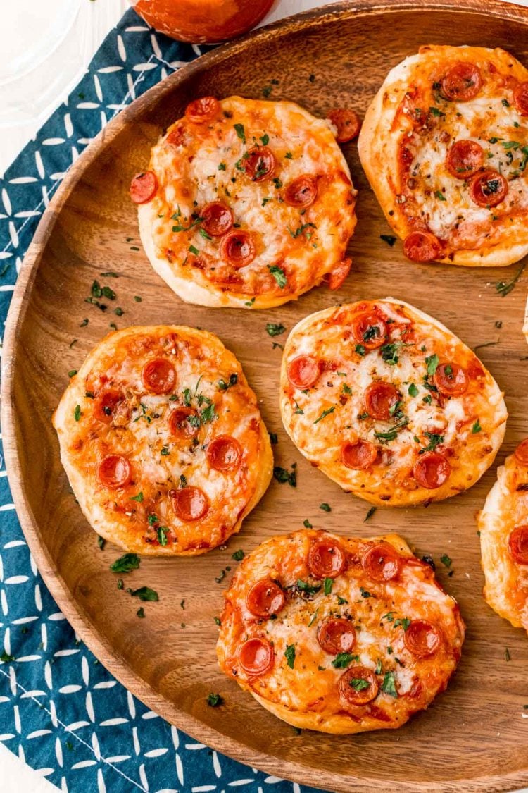 Overhead photo of air fryer pizzas on a wood plate with a blue napkin.