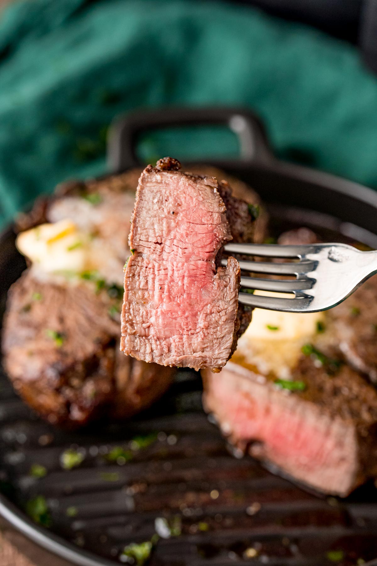 A fork with a piece of steak on it being held towards the camera.