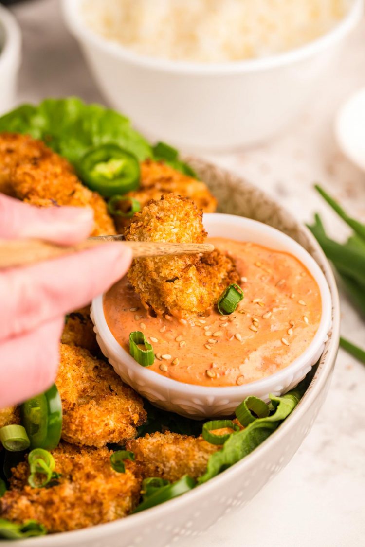A piece of crispy shrimp being dipping in a sauce.