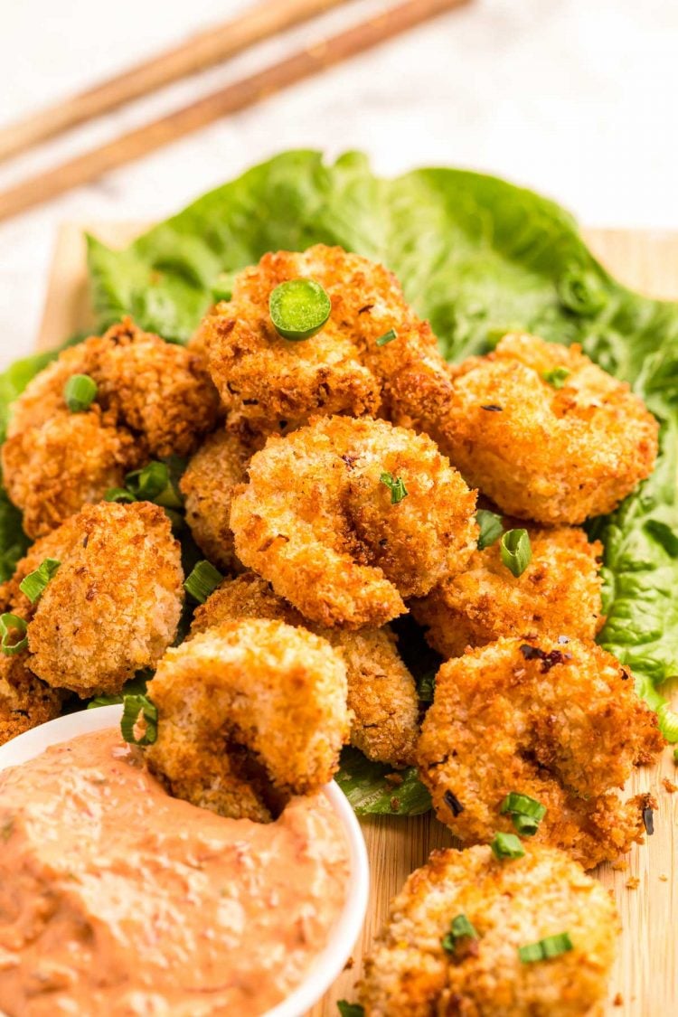 Close up photo of crispy air fryer shrimp on a bed of lettuce with dipping sauce.