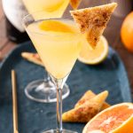 A close up photo of a breakfast martini garnished with cinnamon toast on a blue plate.