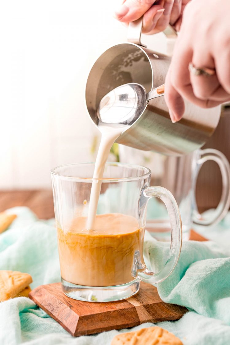 A woman pouring steamed milk into a glass mug with espresso.