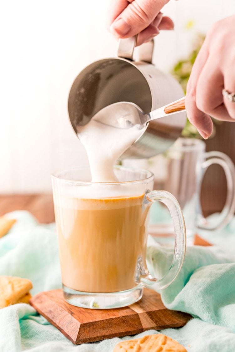 A woman's hand scooping foam out of a milk steaming pitcher onto a latte.