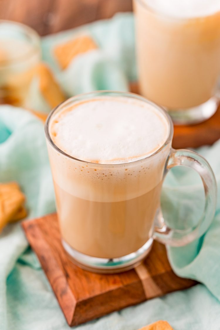 Close up photo of a breve latte in a clear glass mug on a wood coaster.