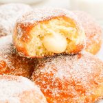 Close up photo of brioche donuts, the top on has a bite missing from it showing vanilla cream inside.