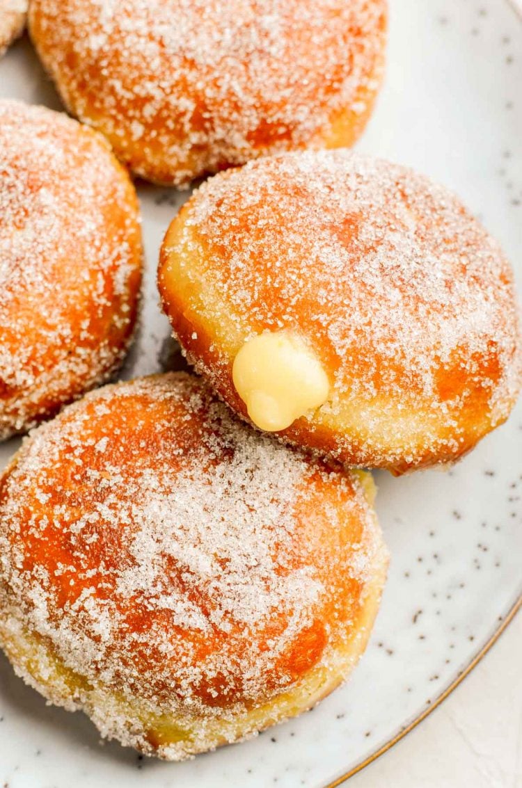 Close up photo of sugared donuts filled with pastry cream on a plate.