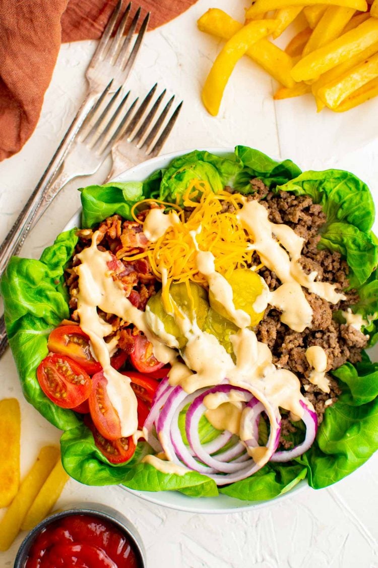 overhead photo of burger bowl with forks next to it and topped with sauce.