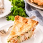 Close up photo of a slice of chicken pot pie on a white plate with a fork.