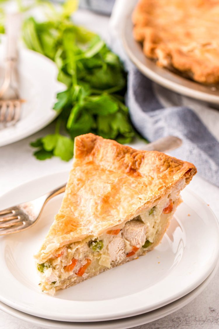 Close up photo of a slice of chicken pot pie on a white plate with a fork.