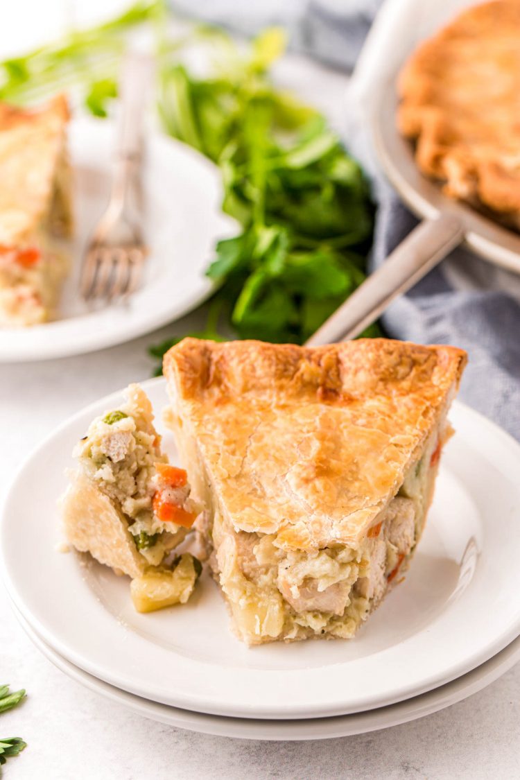 A slice of chicken pot pie on a white plate with a fork with a bite on it.