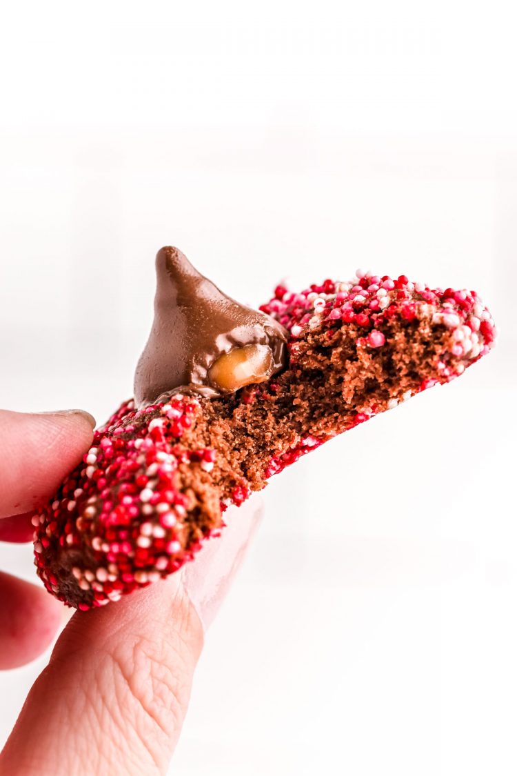 A woman's hand holding up a valentine's day cookies with a hershey kiss with a bite taken out of it.