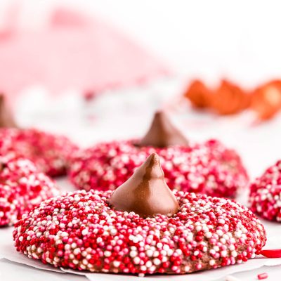 Close up photo of chocolate cookies covered in red, pink, and white sprinkles and topped with a hershey kiss.
