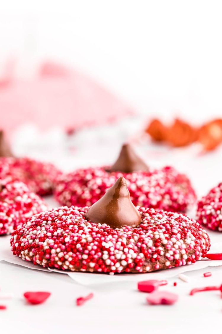 Close up photo of chocolate cookies covered in red, pink, and white sprinkles and topped with a hershey kiss.